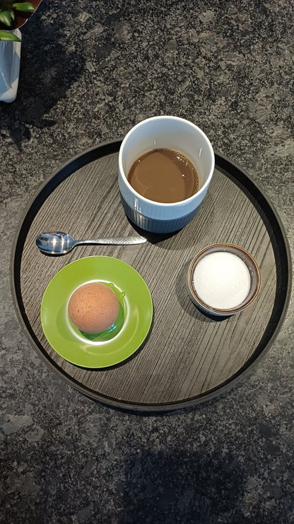 Sort rund 3 D printet ramme, hvori der er lagt en træplade med melaminoverflade, der er afskær fra dansk køkkenproducent. 28 cm i diameter.