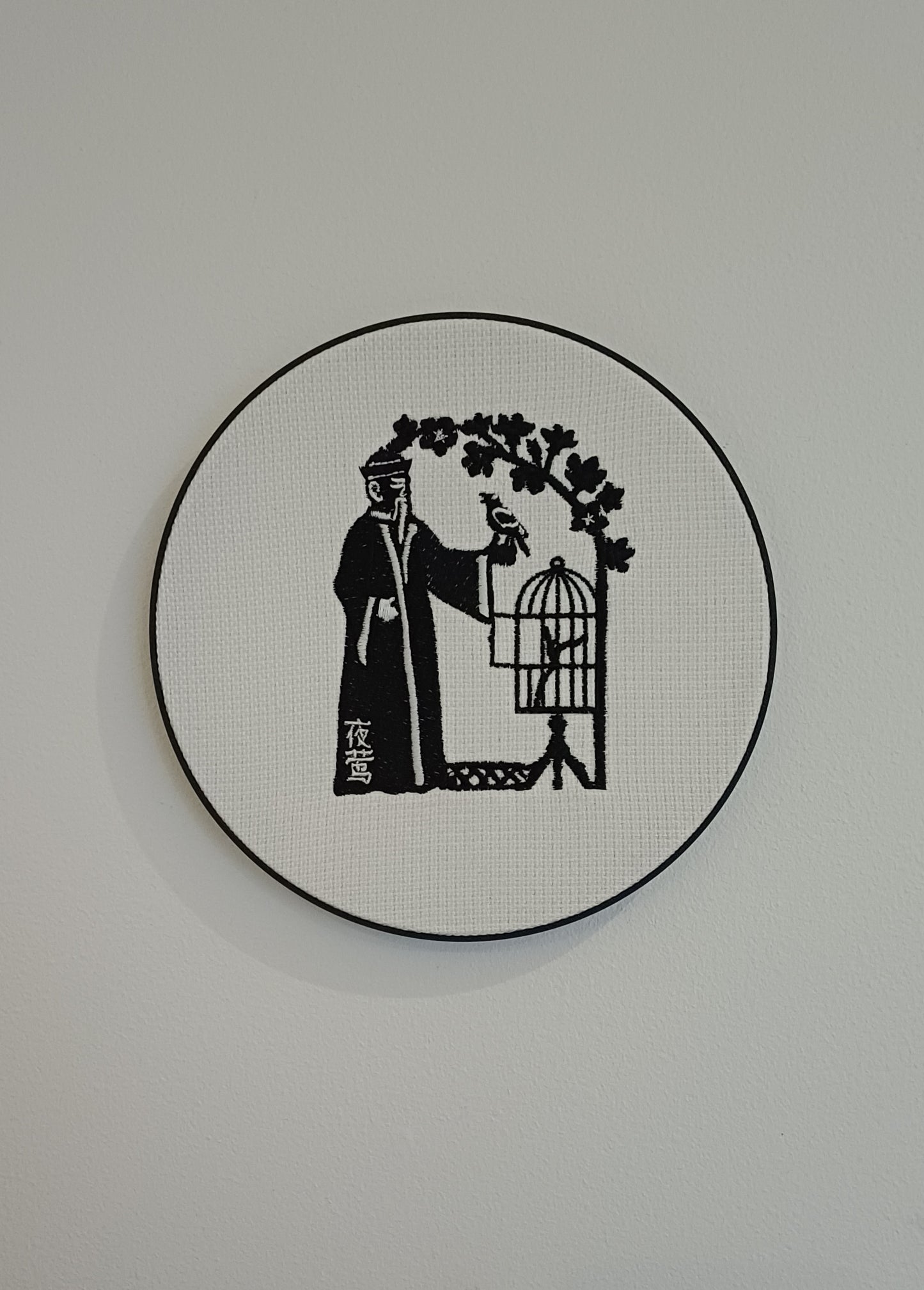 HC Andersens eventyr "nattergalen" som indrammet maskinbroderet motiv med sorte sting på hvid baggrund. Indrammet i sort moderne broderi ramme der måler 20 cm i diameter.