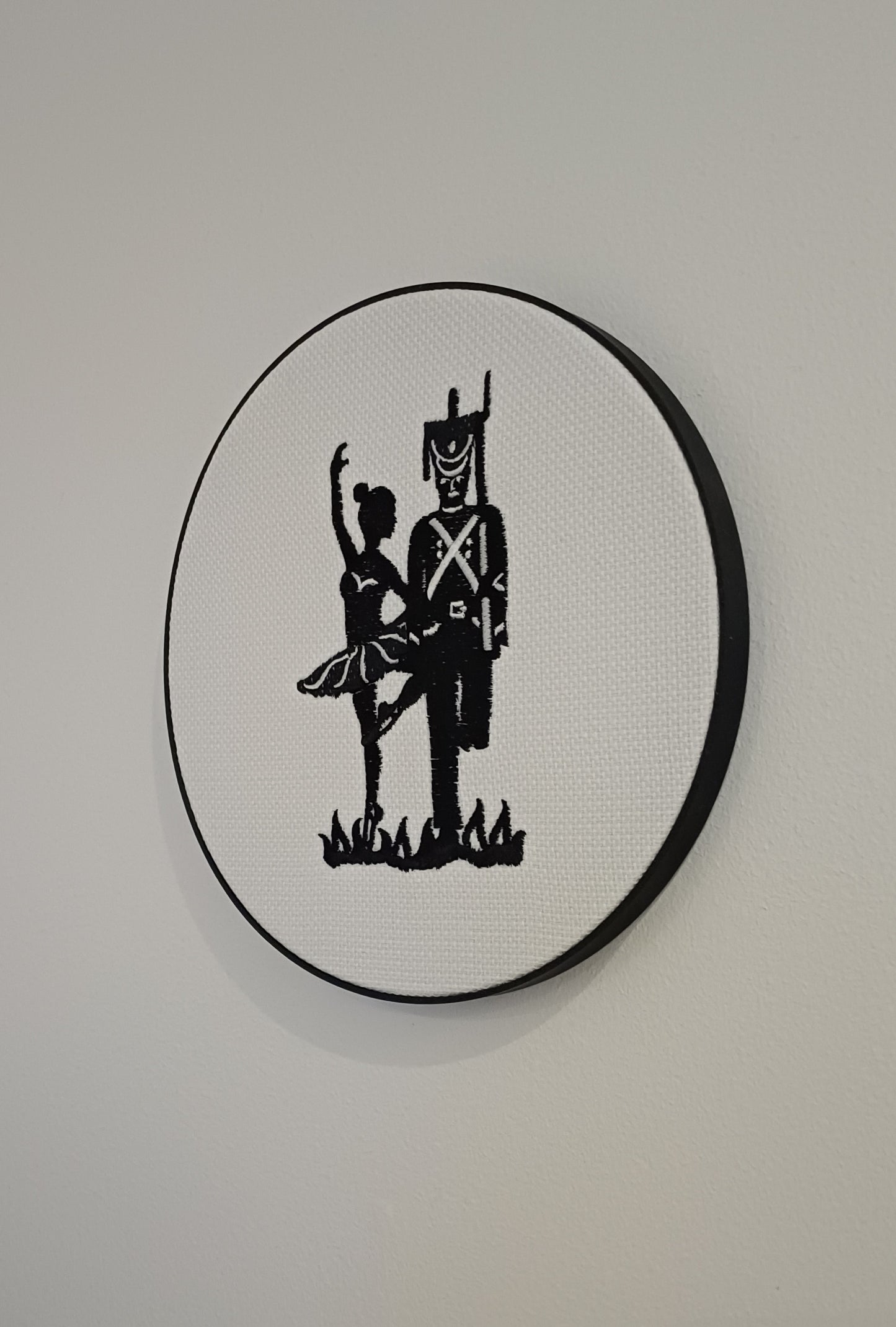 HC Andersens eventyr "Den standhaftige tinsoldat" som indrammet maskinbroderet motiv med sorte sting på hvid baggrund. Indrammet i sort moderne broderi ramme der måler 20 cm i diameter.