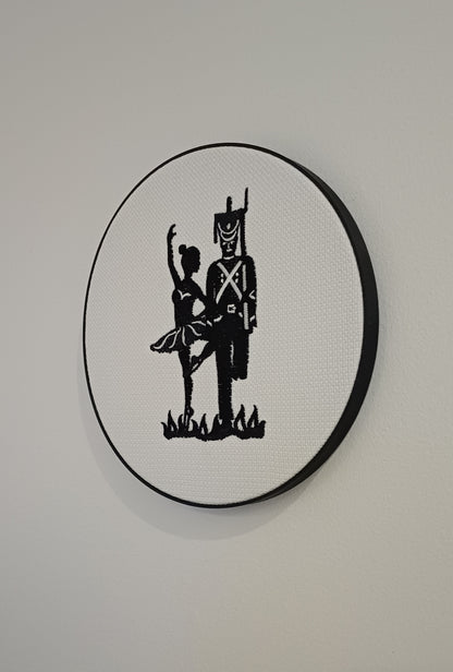 HC Andersens eventyr "Den standhaftige tinsoldat" som indrammet maskinbroderet motiv med sorte sting på hvid baggrund. Indrammet i sort moderne broderi ramme der måler 20 cm i diameter.